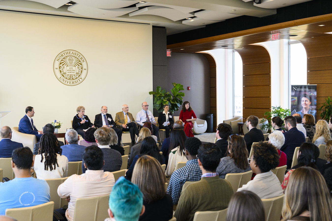 At Northeastern's Khoury College's 40th anniversary, seven people are sitting in front of a large crowd. 