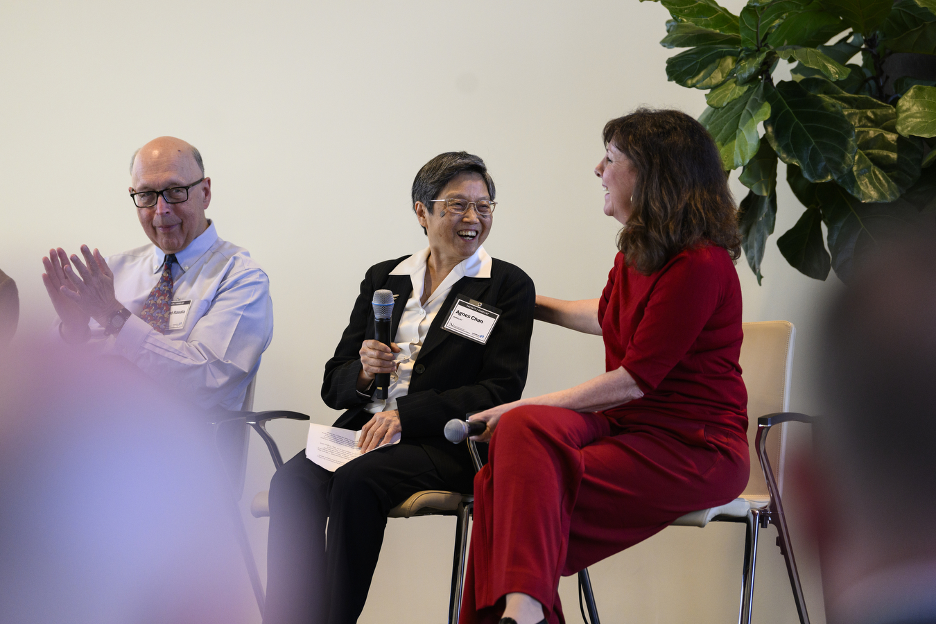 Three people are sitting in front of a crowd while laughing. 