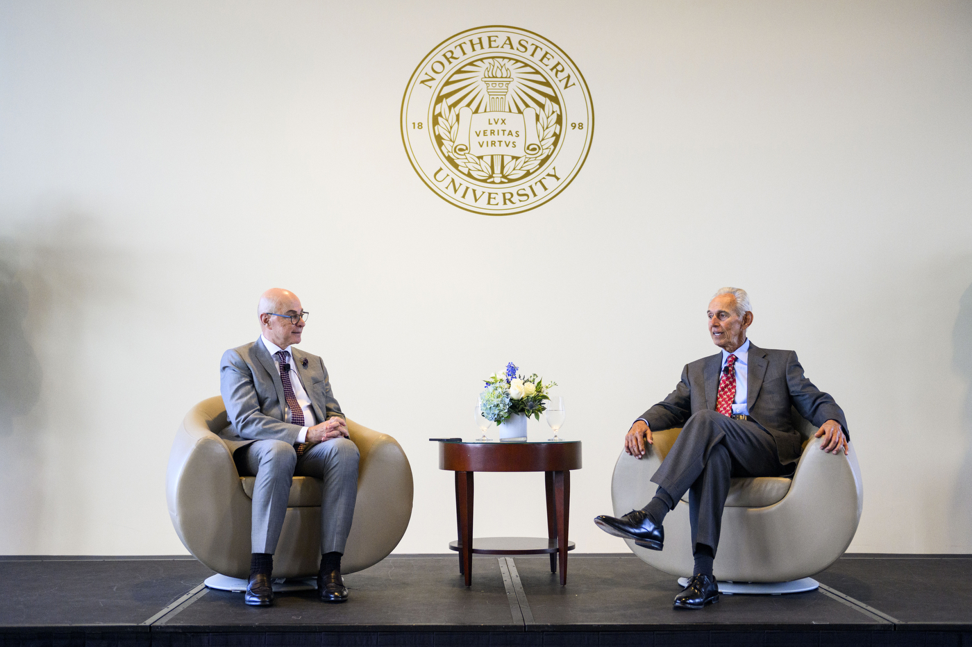 At Northeastern's Khoury College's 40th anniversary, two people are talking next to a small wooden table.