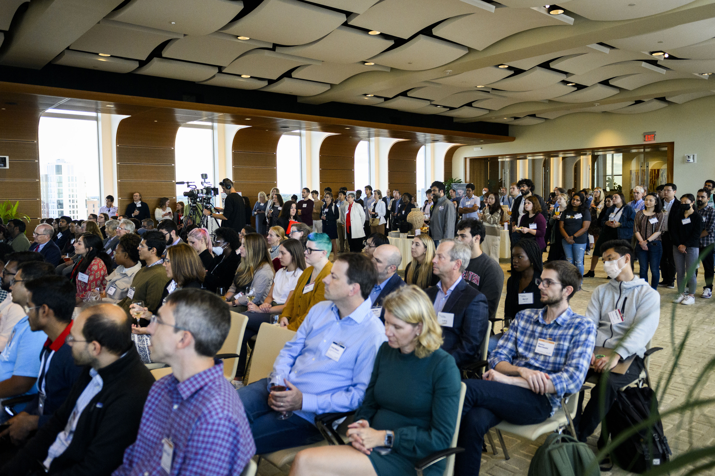 A large crowd of people is sitting together in a brightly lit room. 