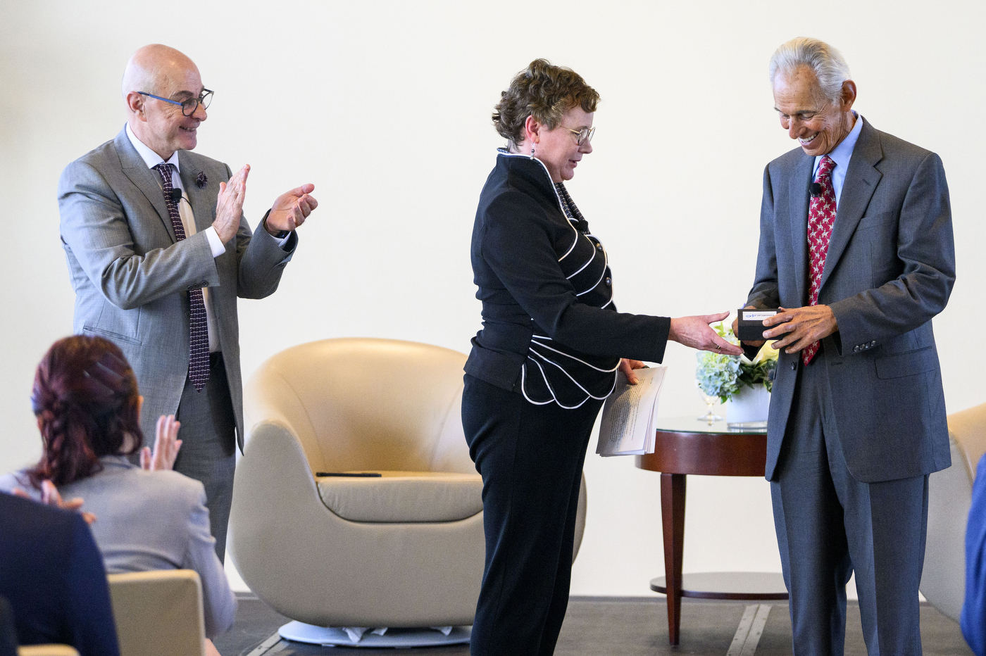 People are clapping as someone in a grey suit is handed an item. 