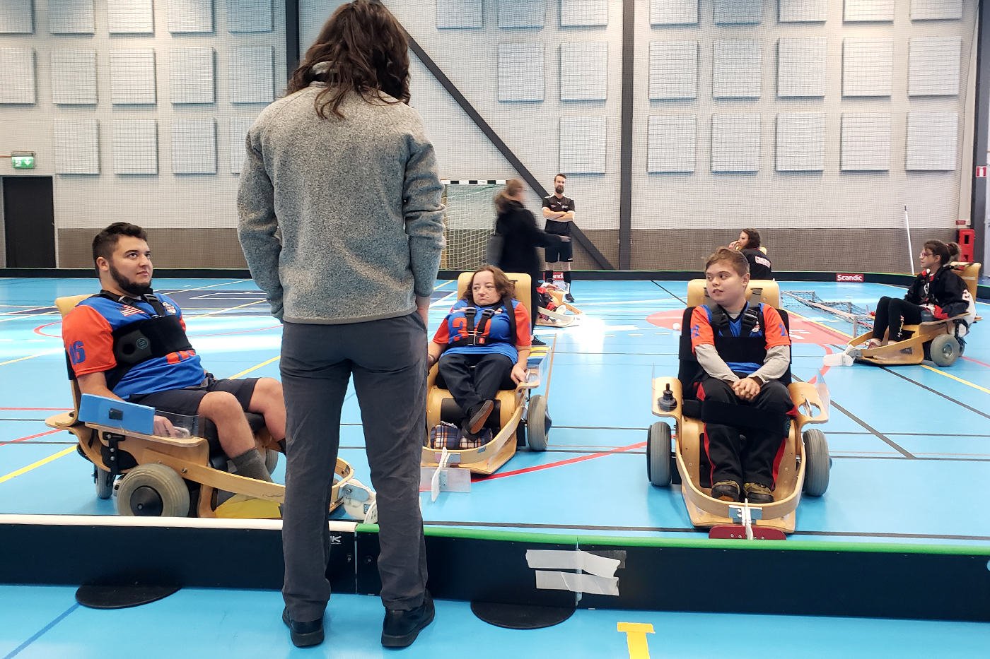 A coach talks to three players on a court in volt hockey chairs