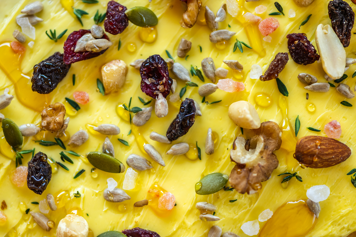 A close-up image of a butter board covered in nuts, honey, and seeds.