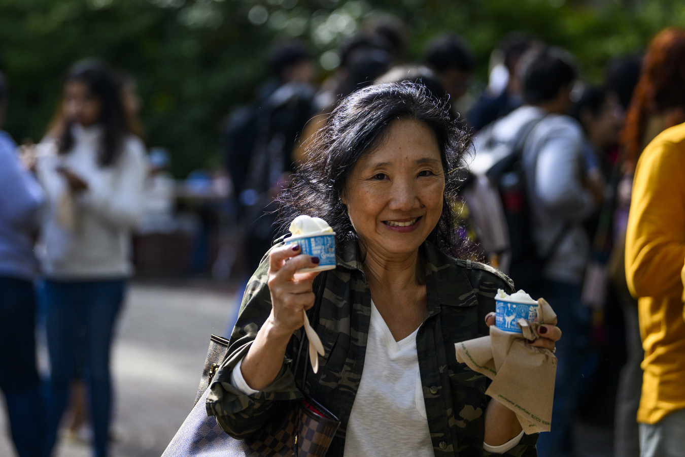 A person is holding two cups of ice cream while walking outside.