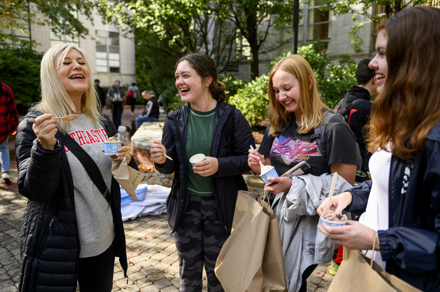 Four people laughing and eating ice cream while standing together in a circle.