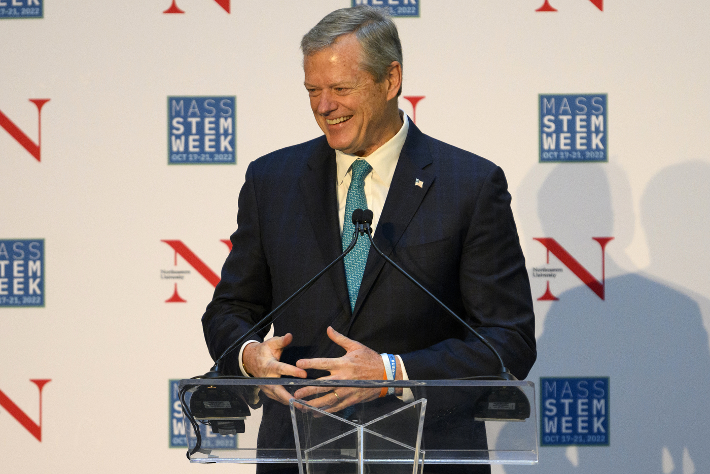 A person wearing a suit stands at a glass podium while talking. 