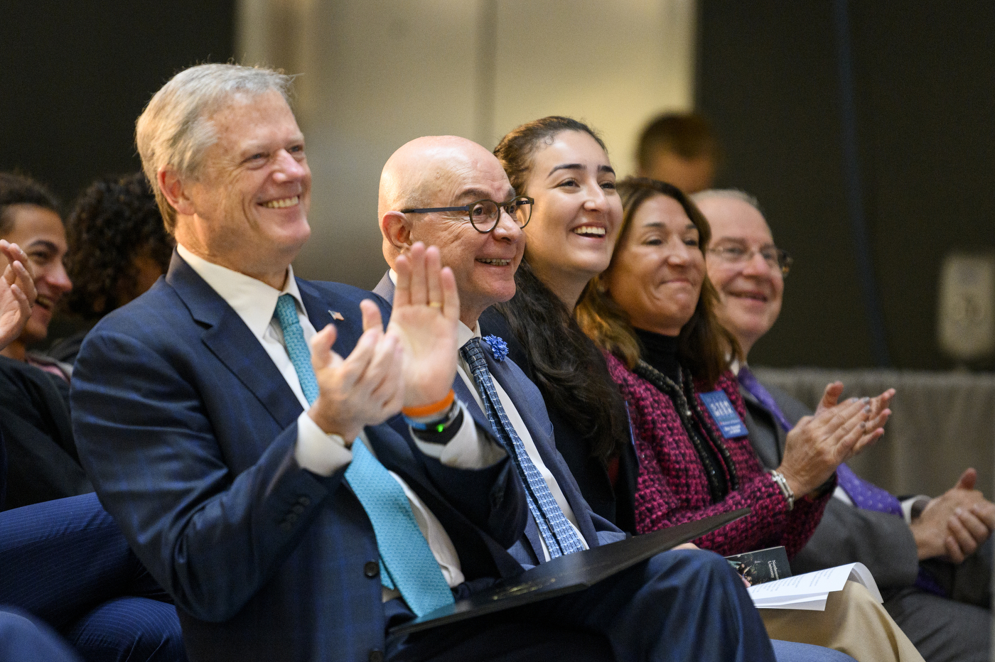 Five people are sitting together while clapping and laughing. 