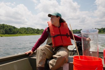 woman steering boat wearing life jacket and baseball hat