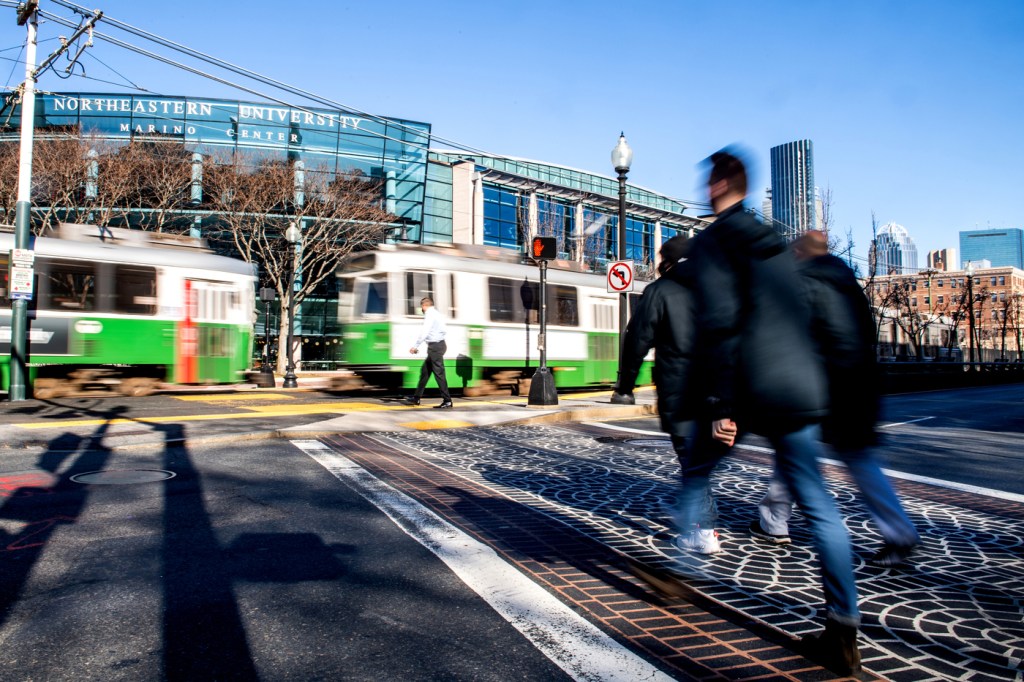 people crossing a street in front of a public transportation stop