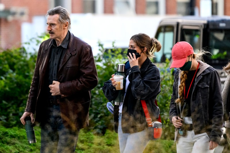 liam neeson walking in front of two masked assistants