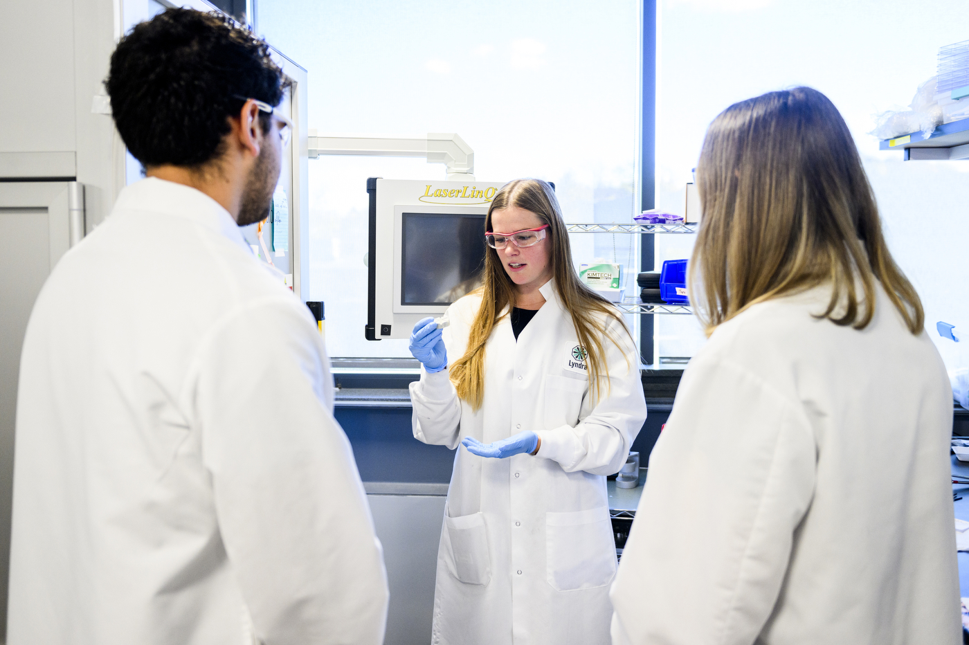 Sarah Liebler working with two other people in white lab coats