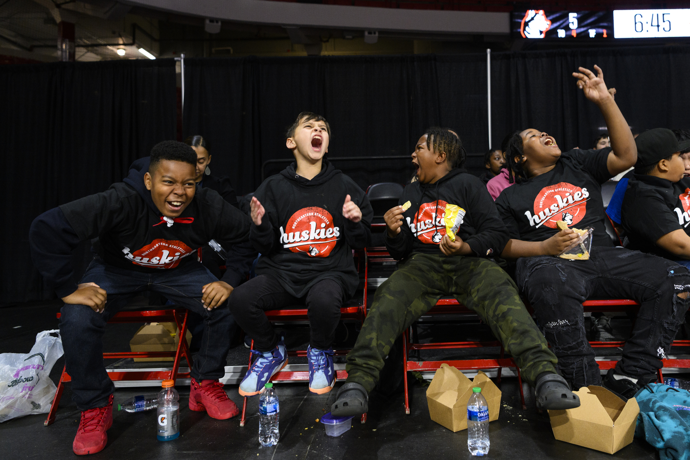 four students cheering loudly courtside at womens basketball game