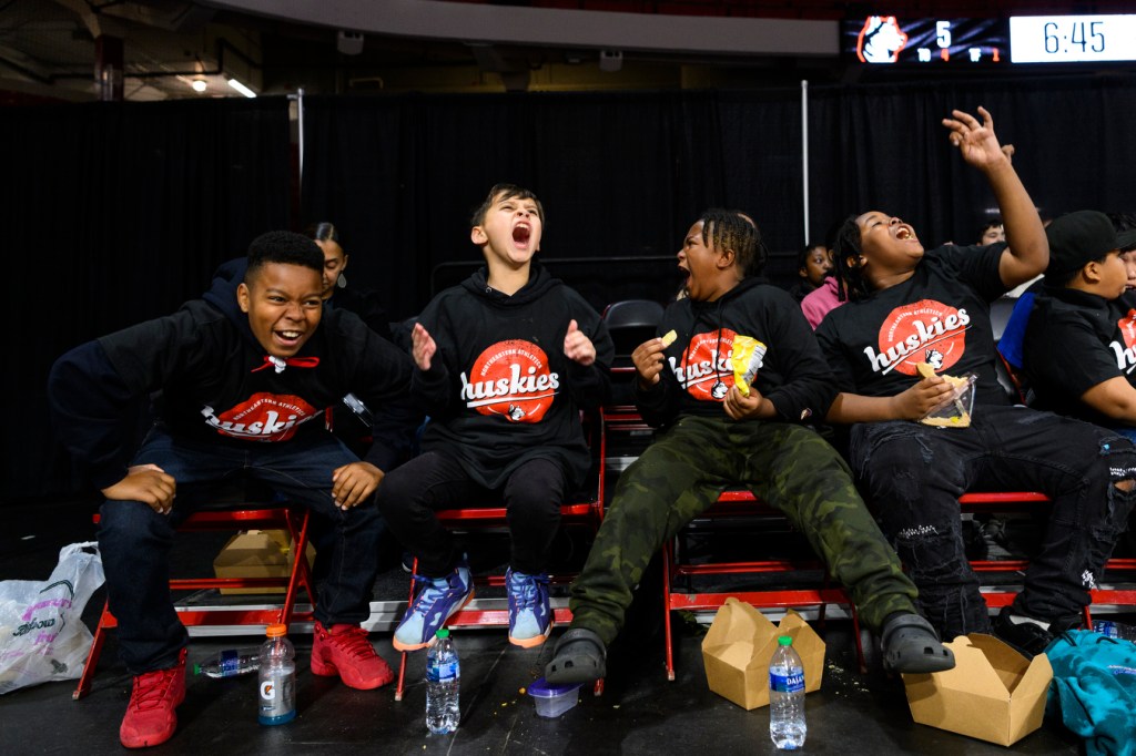 four students cheering loudly courtside at womens basketball game