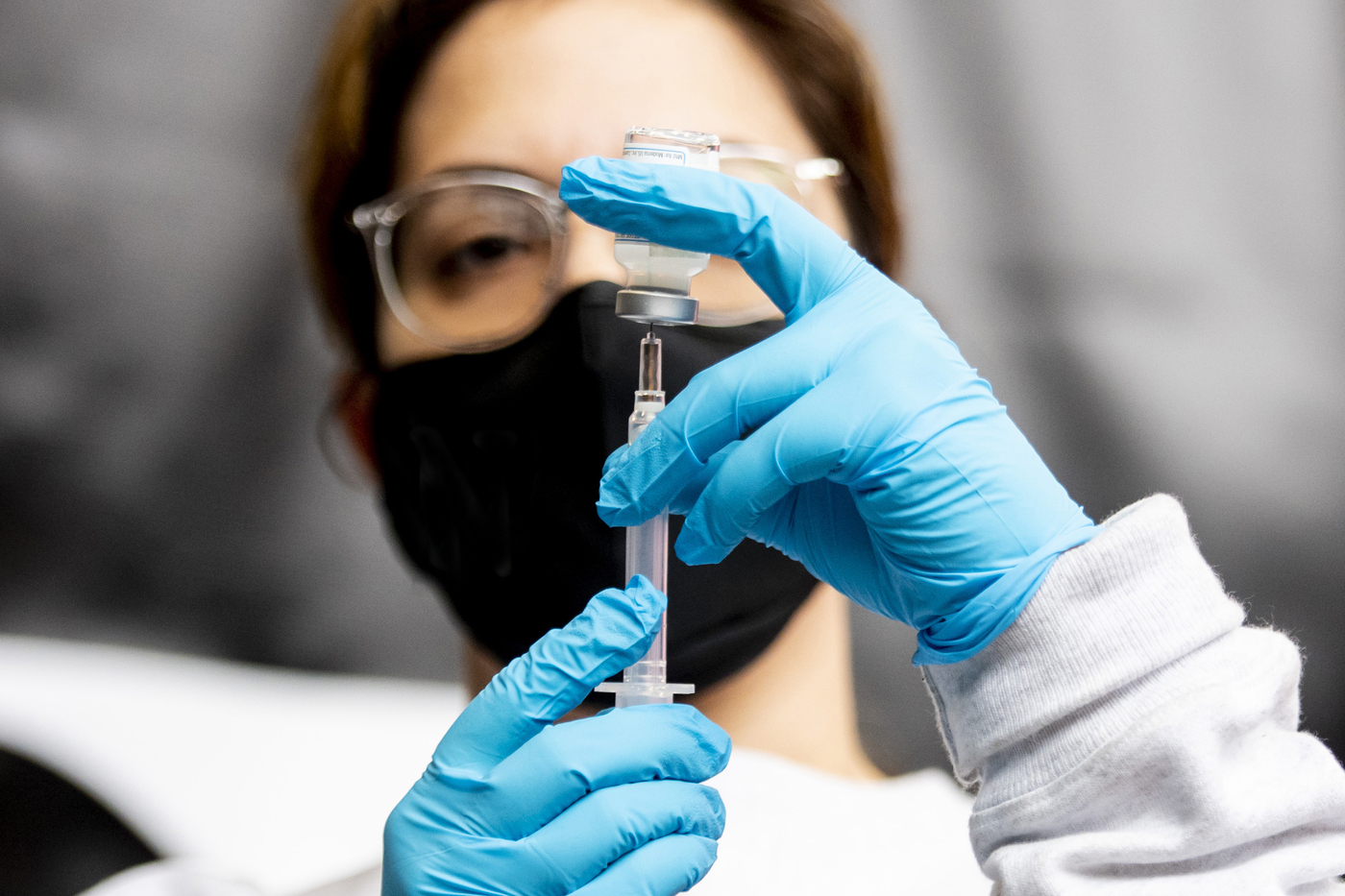 A masked health worker drawing a dose from a vaccine bottle