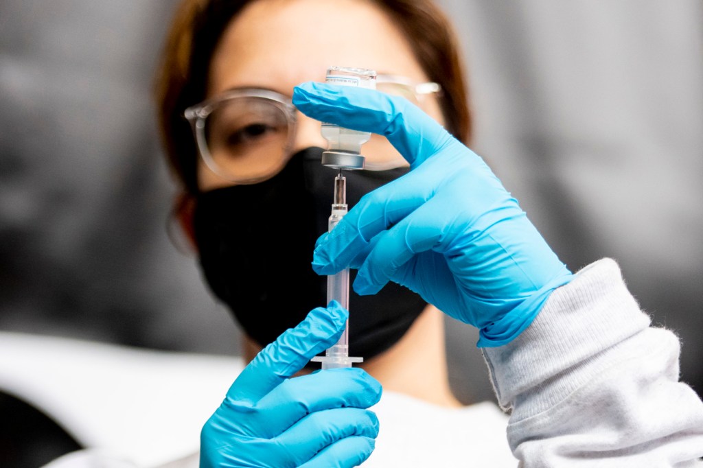 person holding vaccine vial with gloved hands