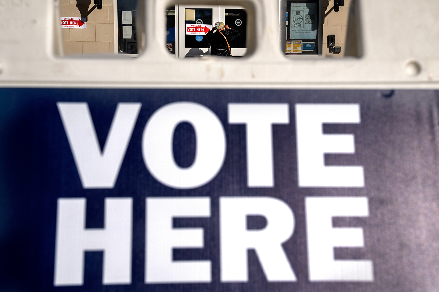 A sandwich board saying 'VOTE HERE' with someone entering a building in the background