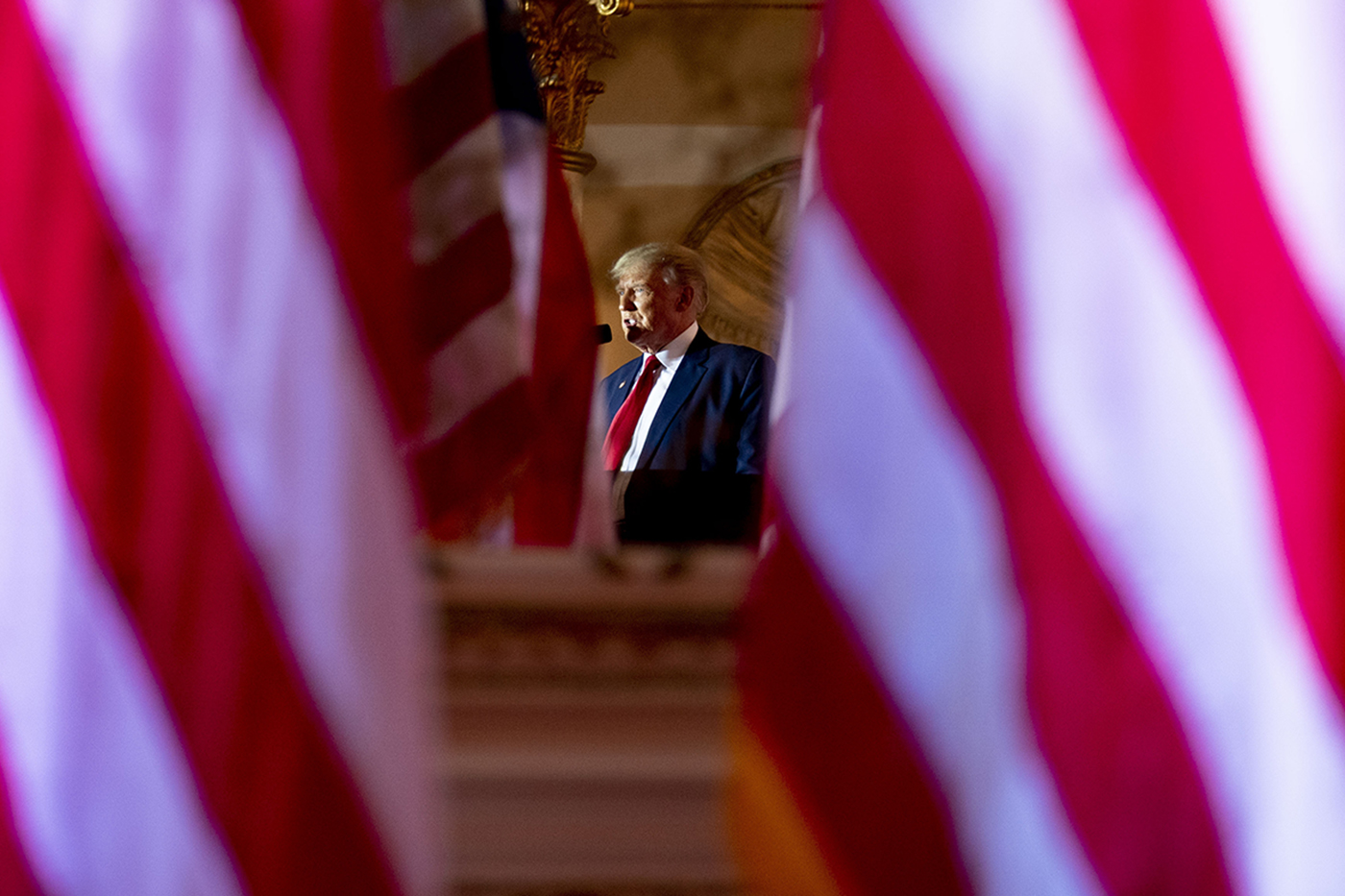 Trump speaking at a podium flanked by American flags