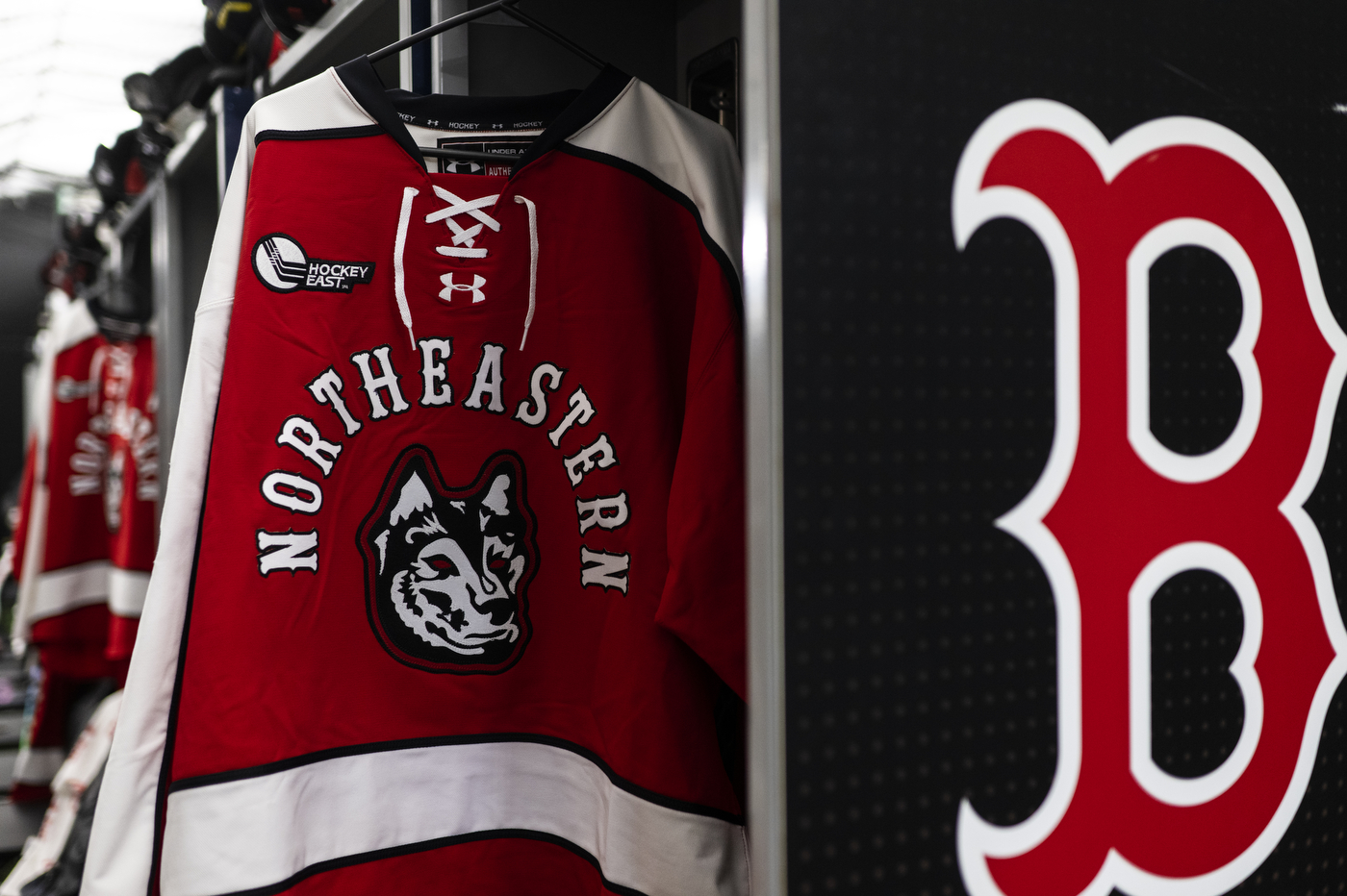 A Northeastern hockey jersey in red, black, and white colors hangs from a rack. 