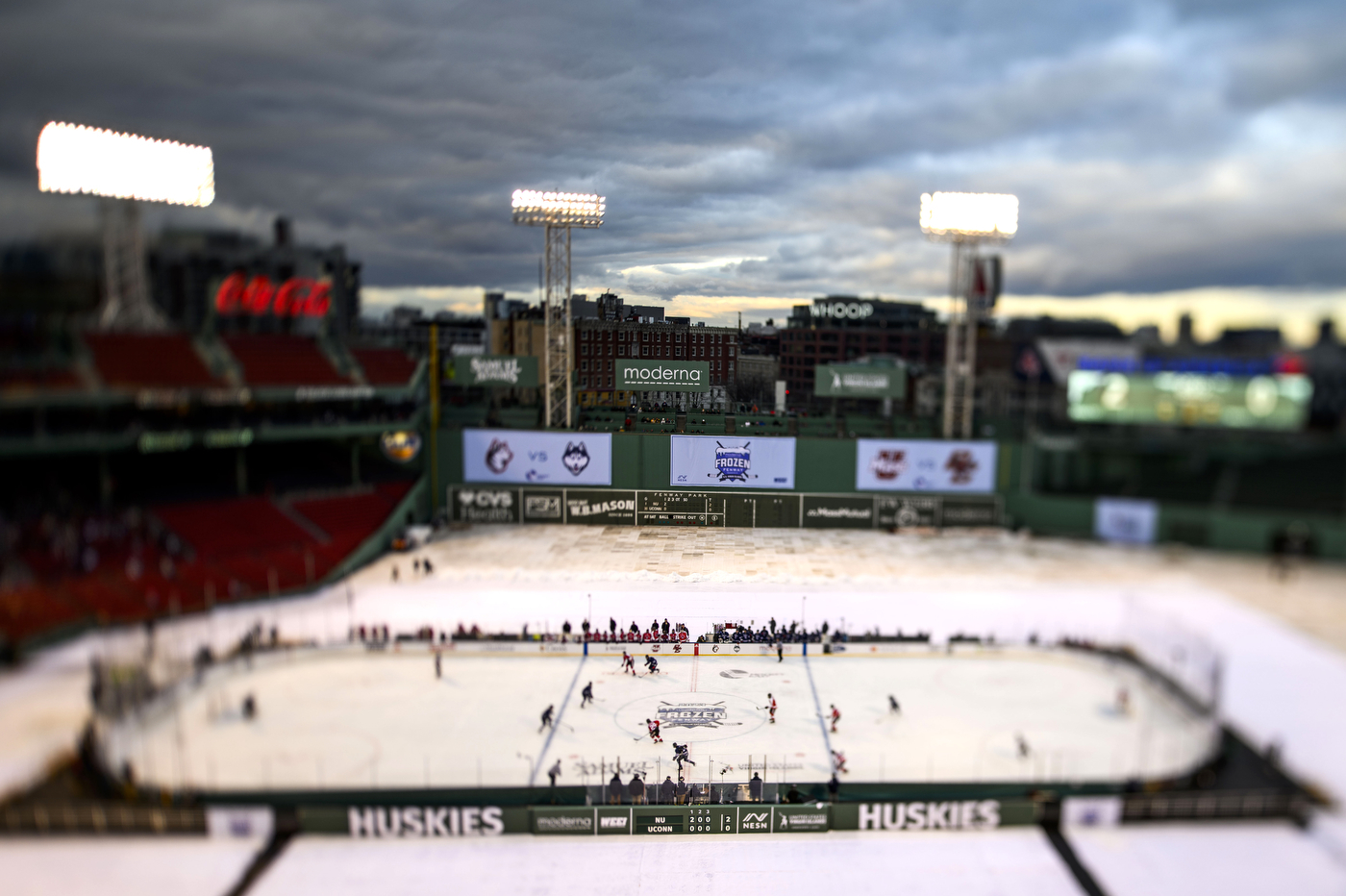 Hockey players playing on an ice skating rink in the middle of Fenway Park. 