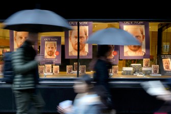 people carrying umbrellas walk past a bookstore window display of prince harry's memoir