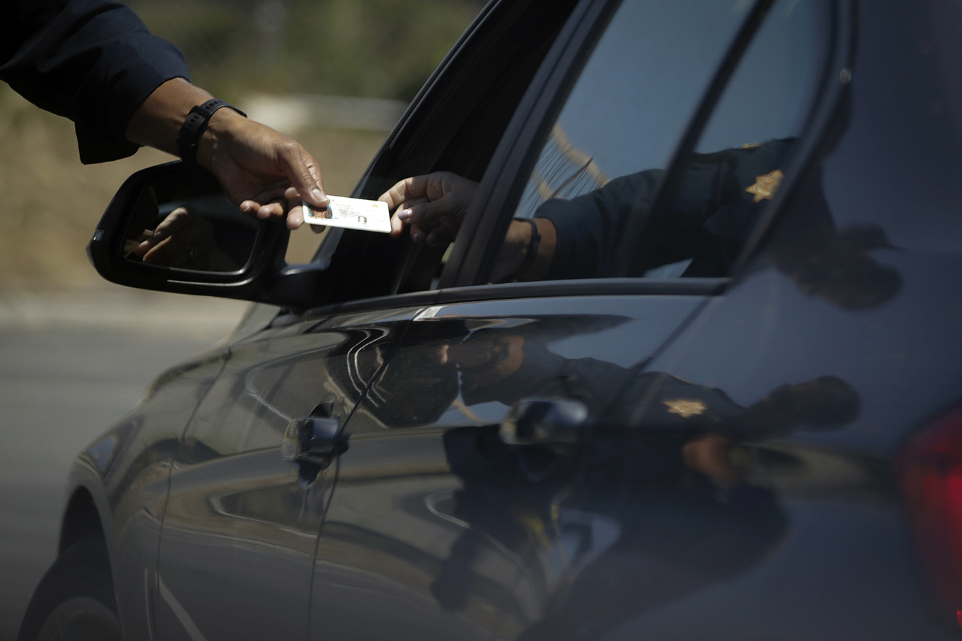 driver handing their ID to a police officer through the window of their car