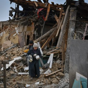 person carrying belongings out of a bombed home