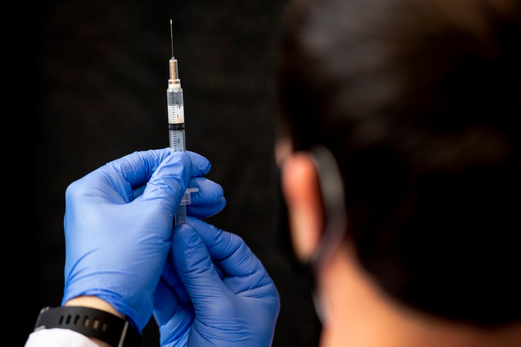 person holding up syringe with gloved hands