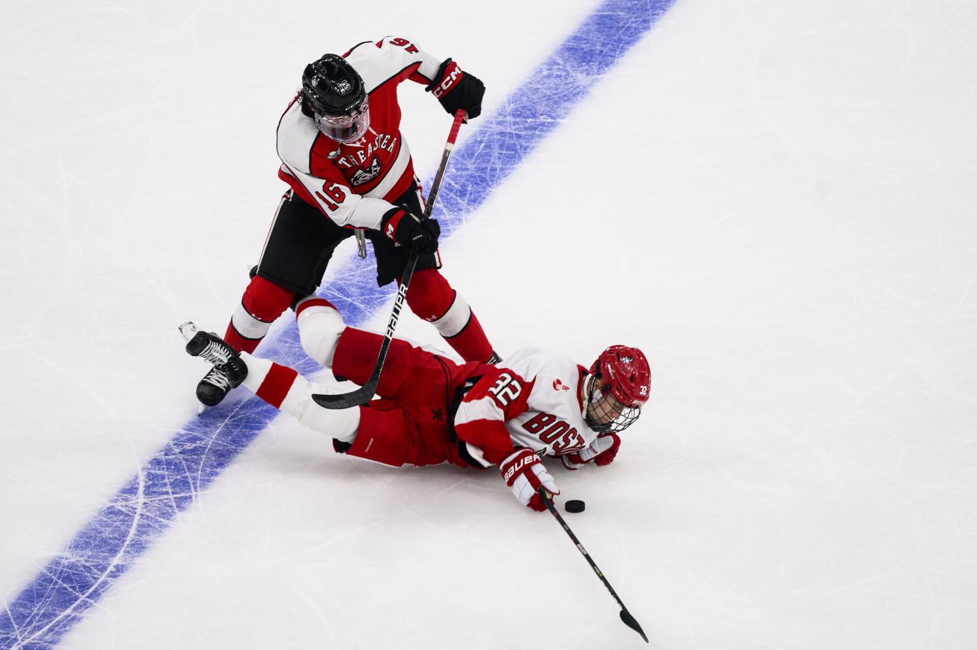 northeastern university hockey player skating over a boston university player as they fall