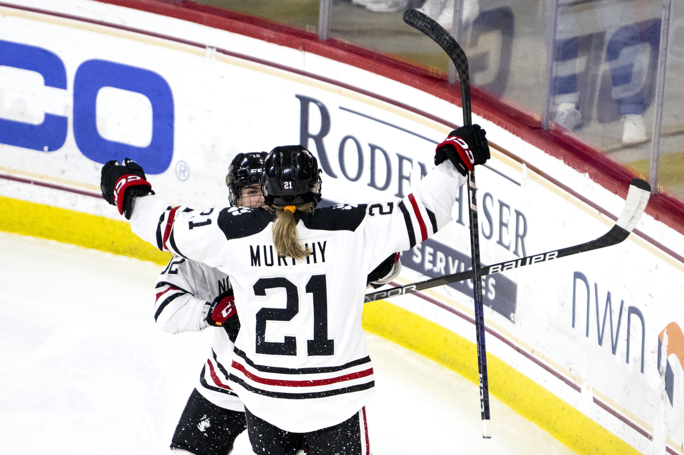 two northeastern hockey teams hugging in celebration