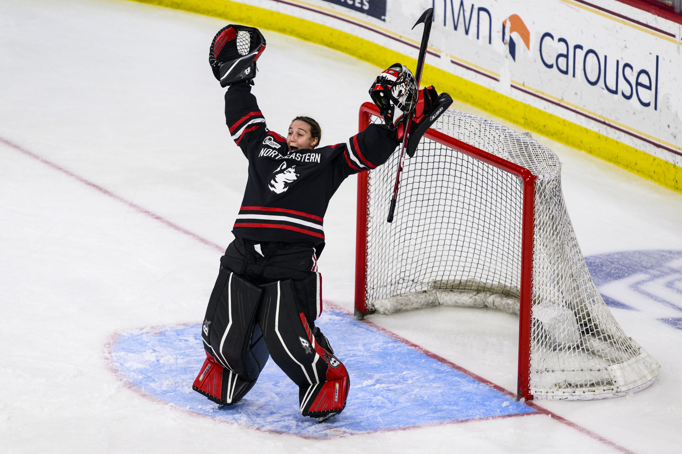 A Northeastern women's hockey goal holders her stick and arms up in celebration