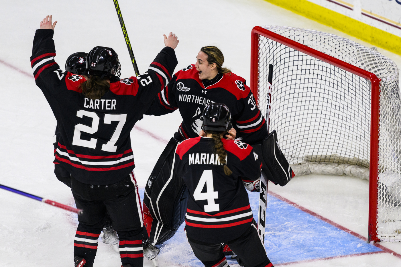 Three hockey players skate towards the goalie in celebration