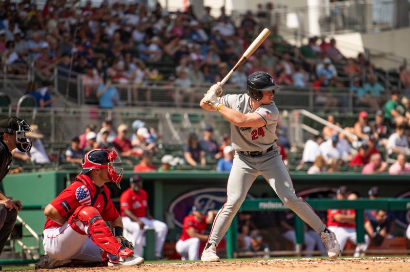 A Northeastern baseball player at the plate ready to receive a pitch with a Red Sox player catching