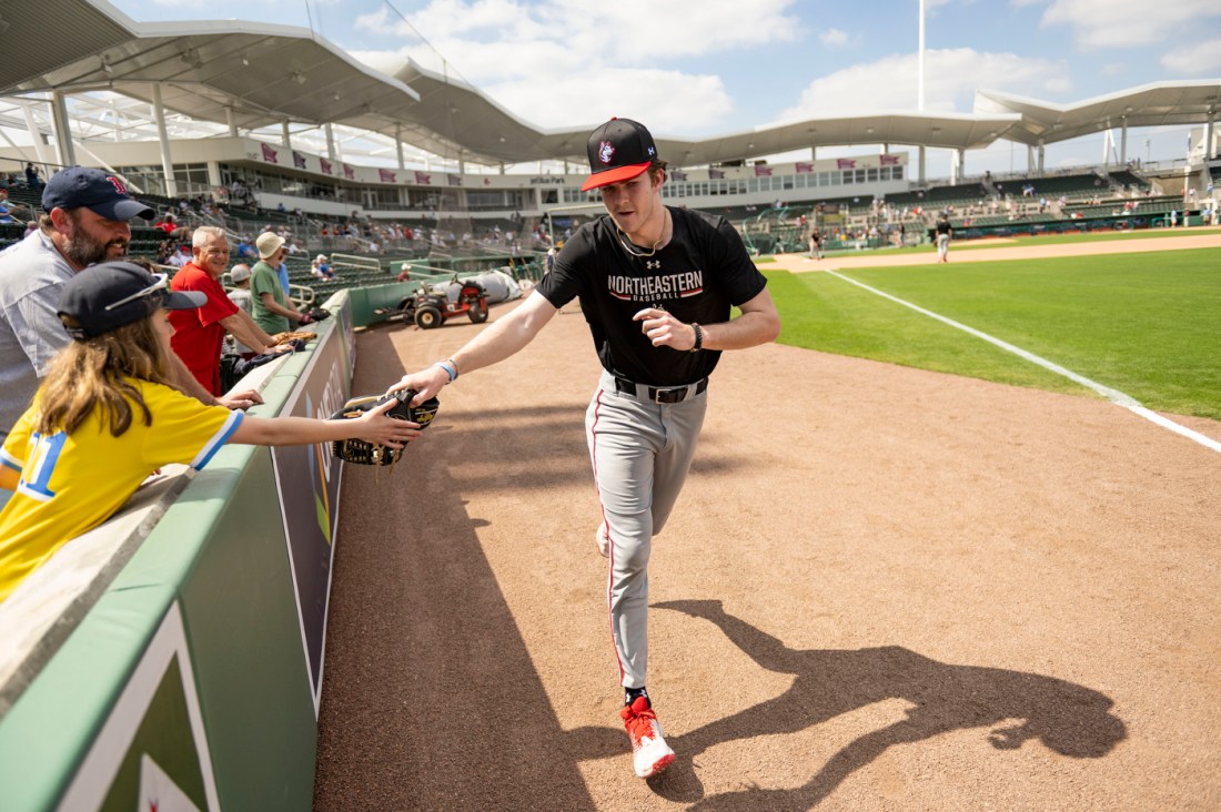 A northeastern baseball player high fives a fan in the stands 