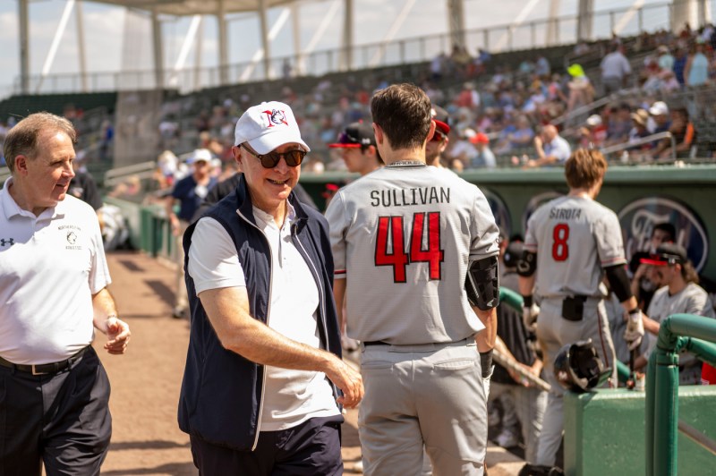 Northeastern University President smiles wearing a Northeastern baseball cap