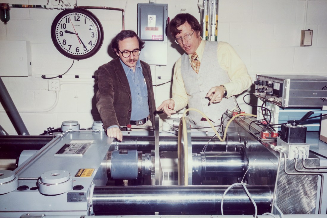 Heyman with a co-worker, pointing to part of a machine