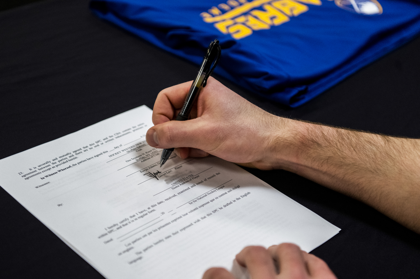 A closeup of Devon signing the contract, pen in hand