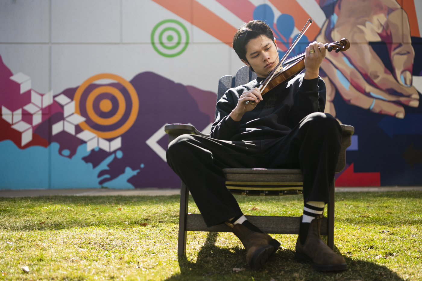 Joe de Georgeo plays the fiddle in front of a mural on Northeastern's Boston campus.