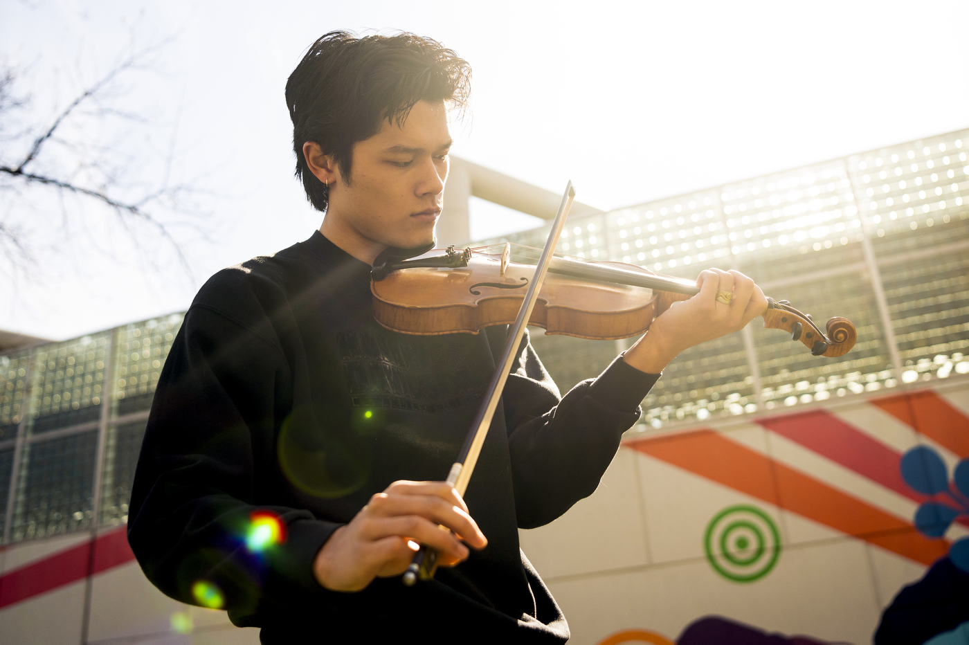 Joe de Georgeo plays the fiddle in front of a mural.