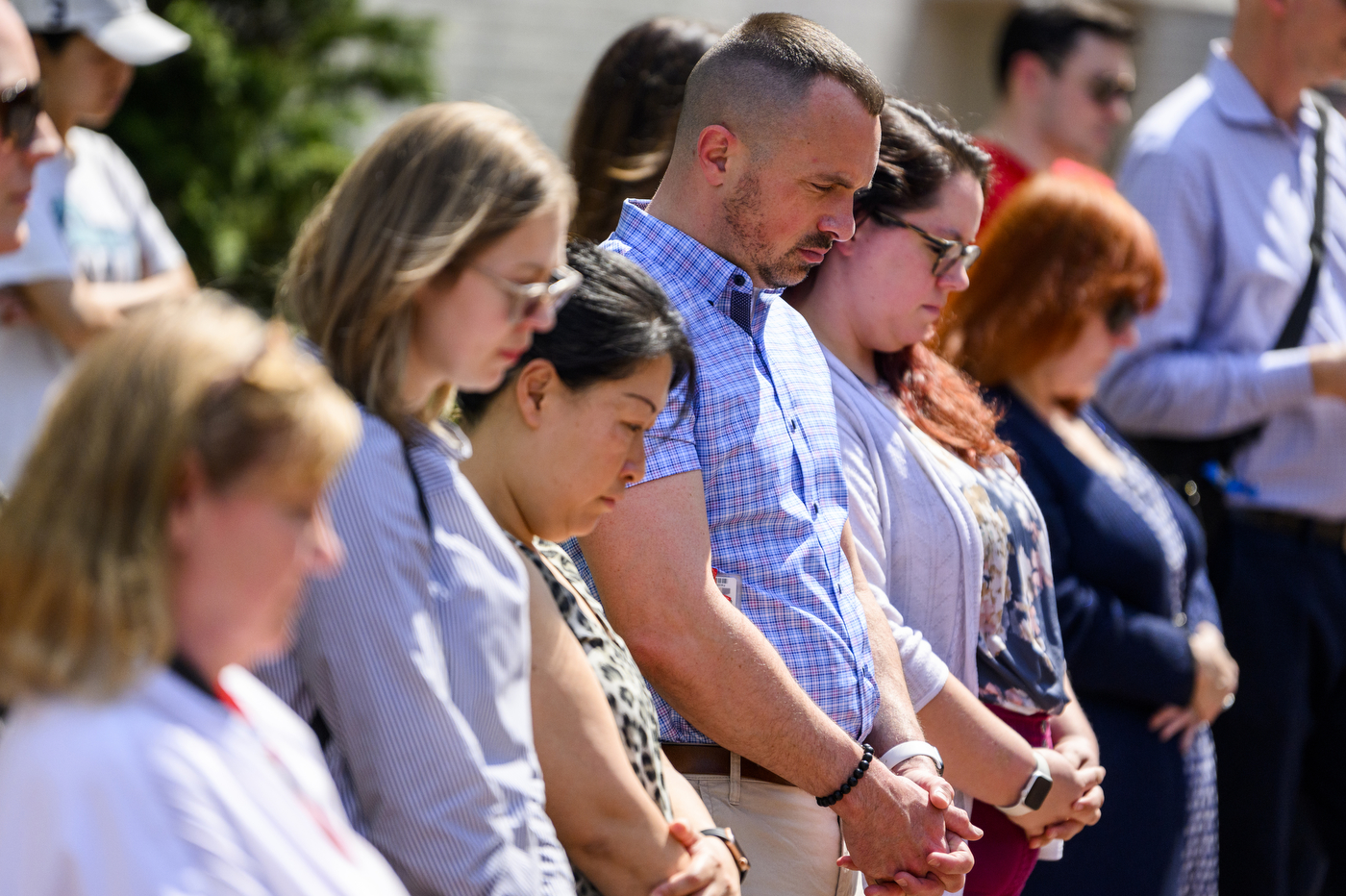 People stand with their hands crossed and heads bowed