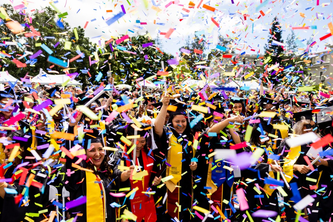 Rainbow confetti falling around a crowd full of graduates outside at Mills College.