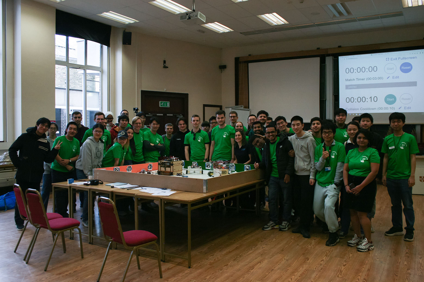 Students posing near a table with  several of their robots at a robotics competition. 