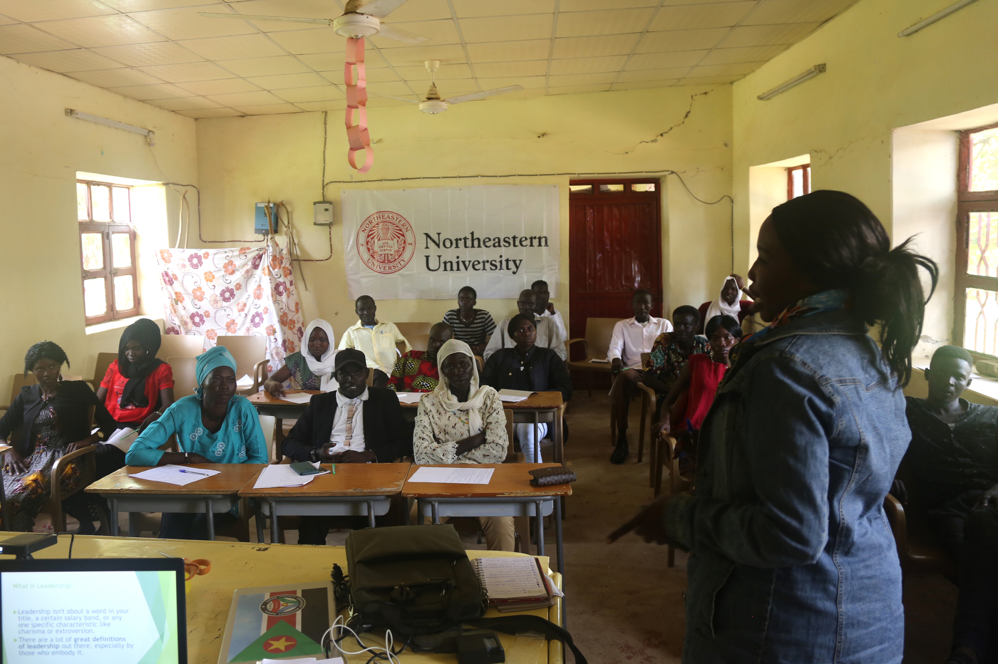 Sudanese people in a classroom with a Northeastern University flag on the wall