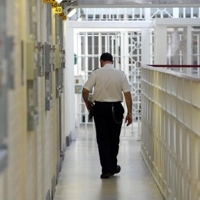 Prison guard walks down a hallway of cells.