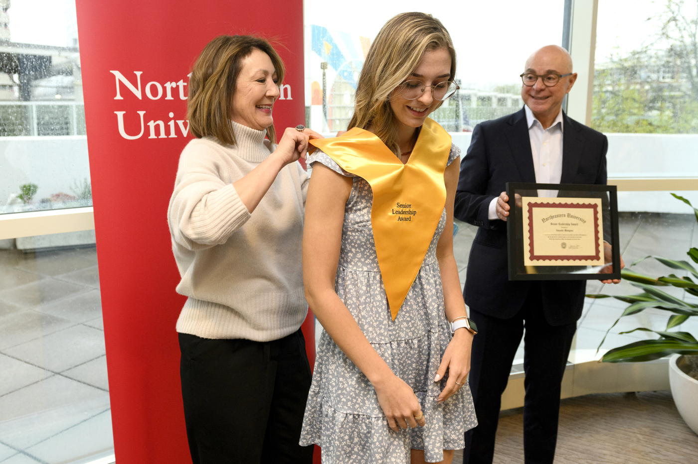 Northeastern student wearing gold sash and holding certificate next to President Aoun