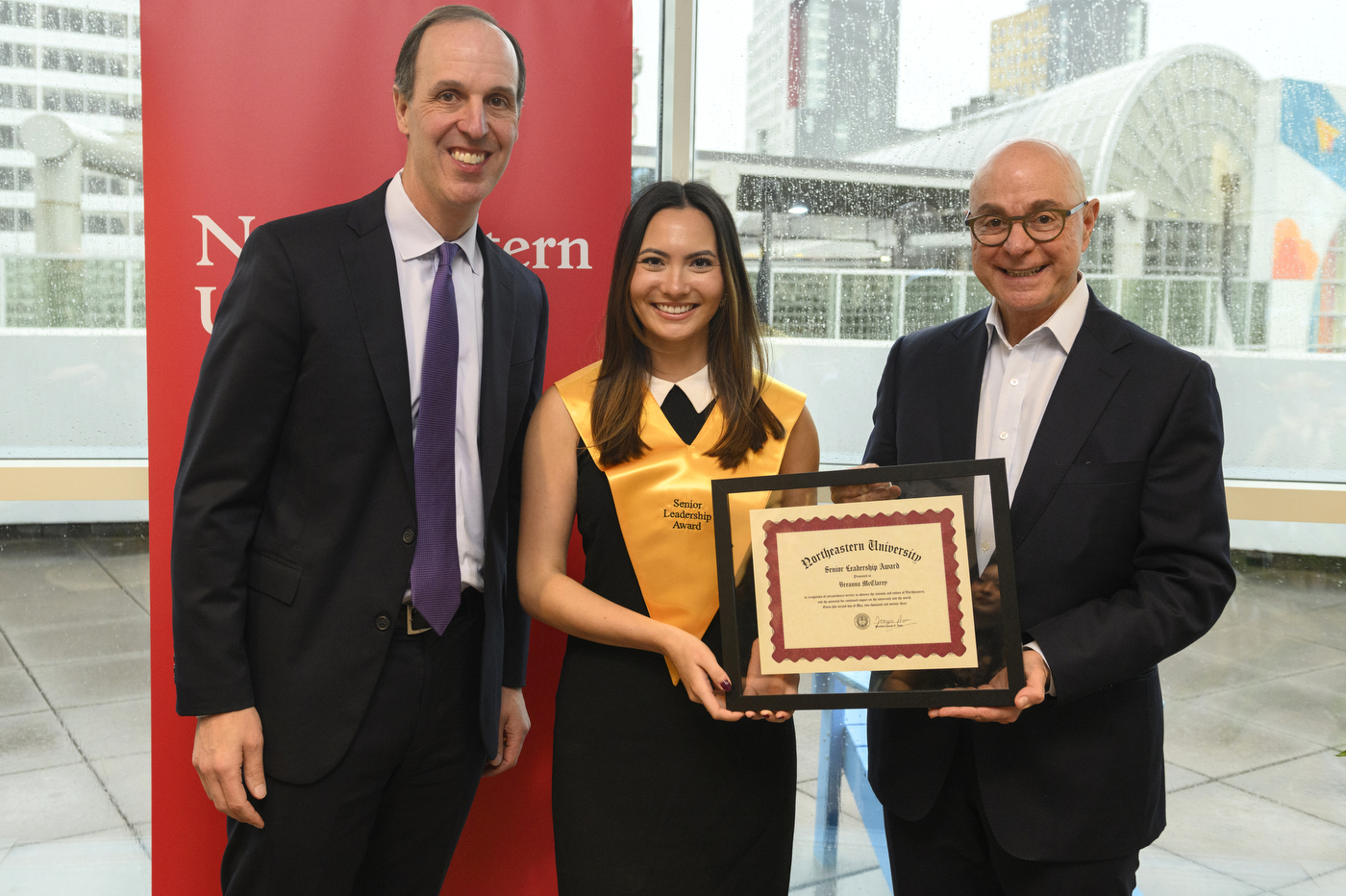 Northeastern student wearing gold sash and holding certificate next to President Aoun