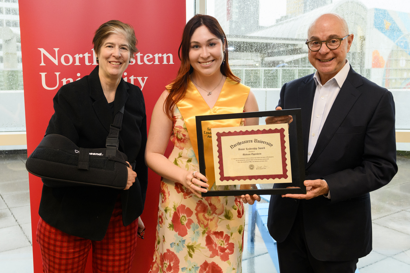 Northeastern student wearing gold sash and holding certificate next to President Aoun