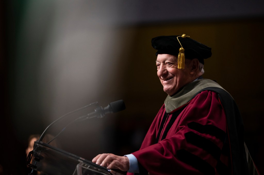 A man in commencement cap and gown delivers a speech