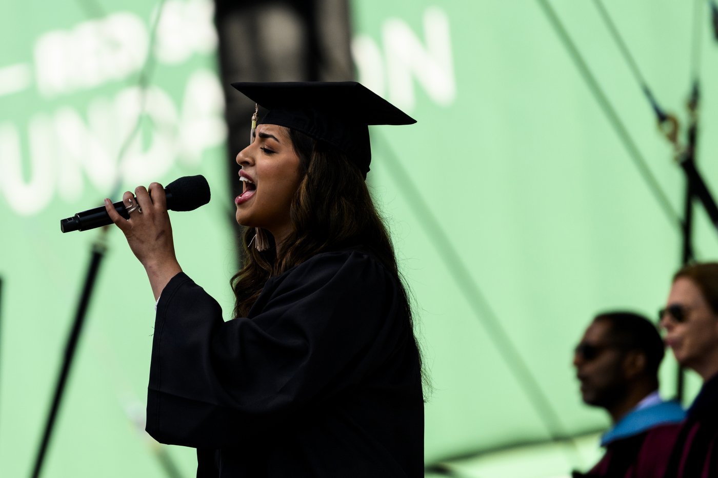 Person singing national anthem in graduation cap and gown