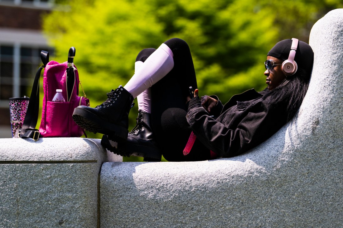 Student sitting on a concrete structure with headphones and sunglasses on. 