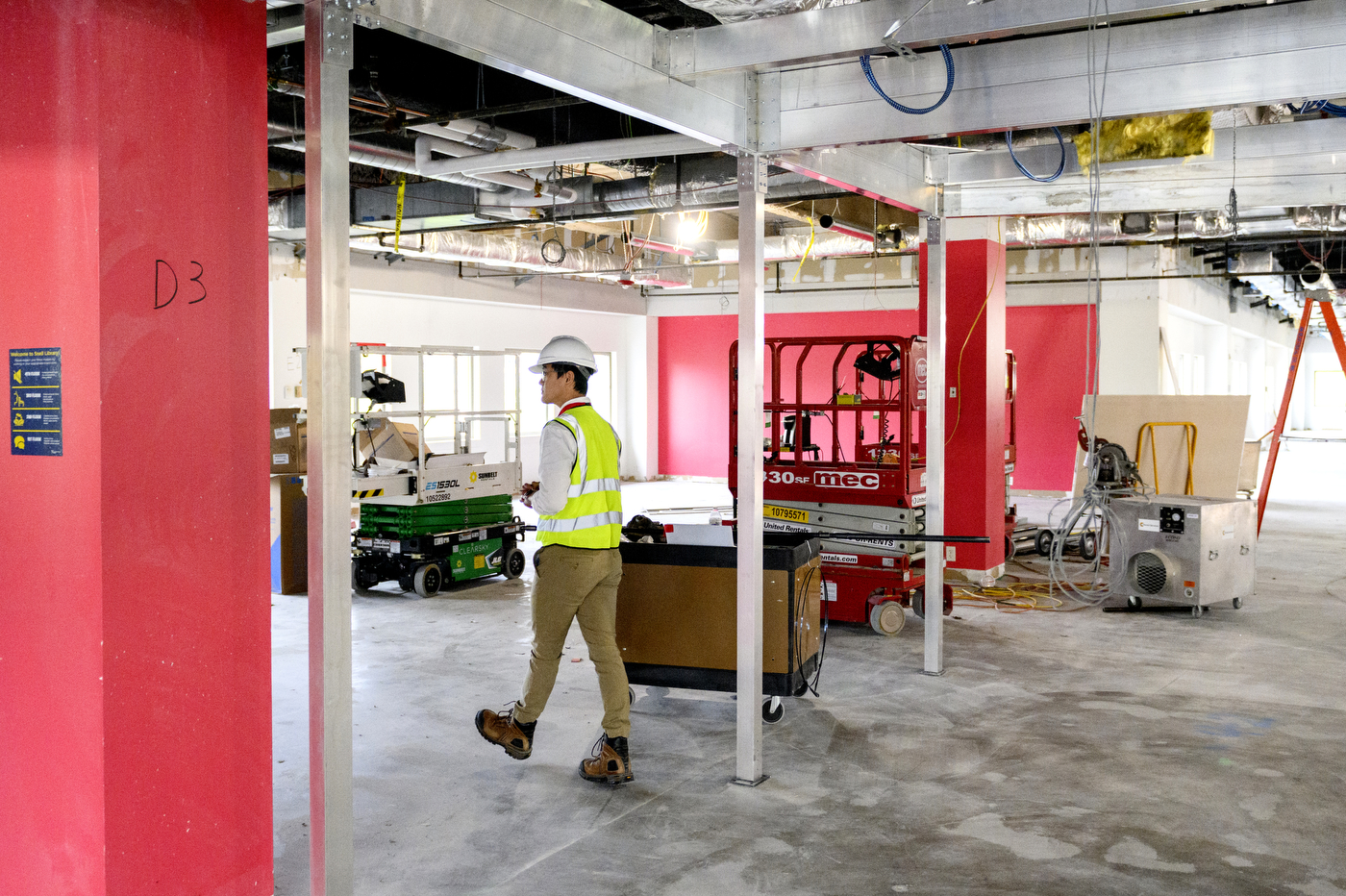 man wearing hard had and reflective vest walking through snell library room under construction